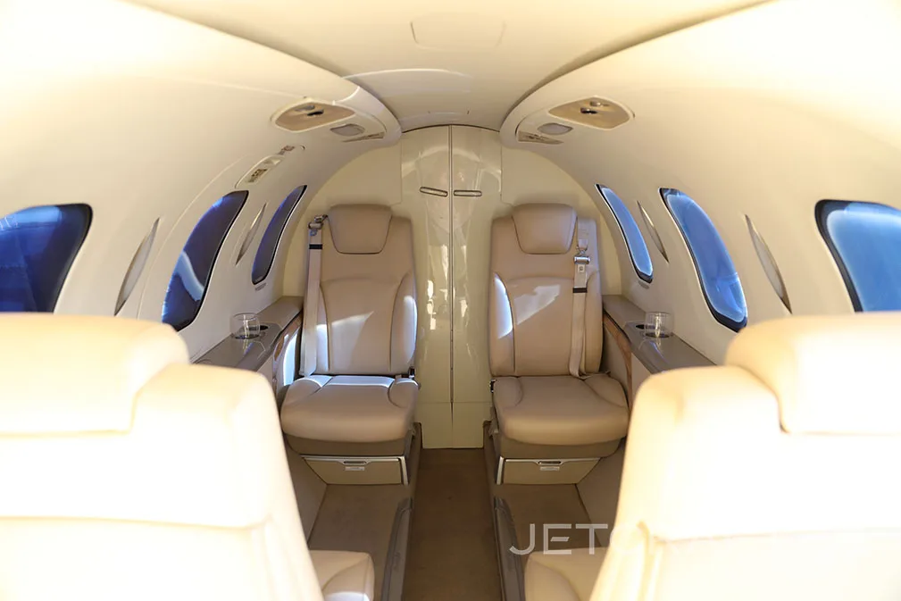 The interior cabin of a private jet features beige leather seats and a central aisle.