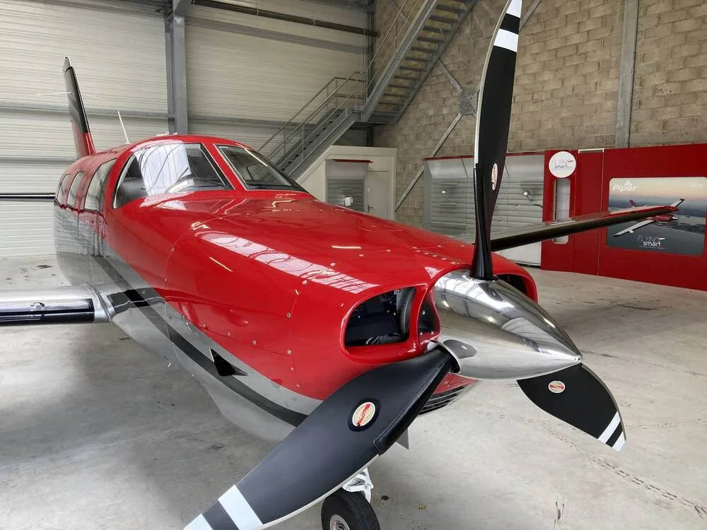 A close-up view of the propeller and nose of a red and silver Piper M350 aircraft, N350XT, in a hangar.