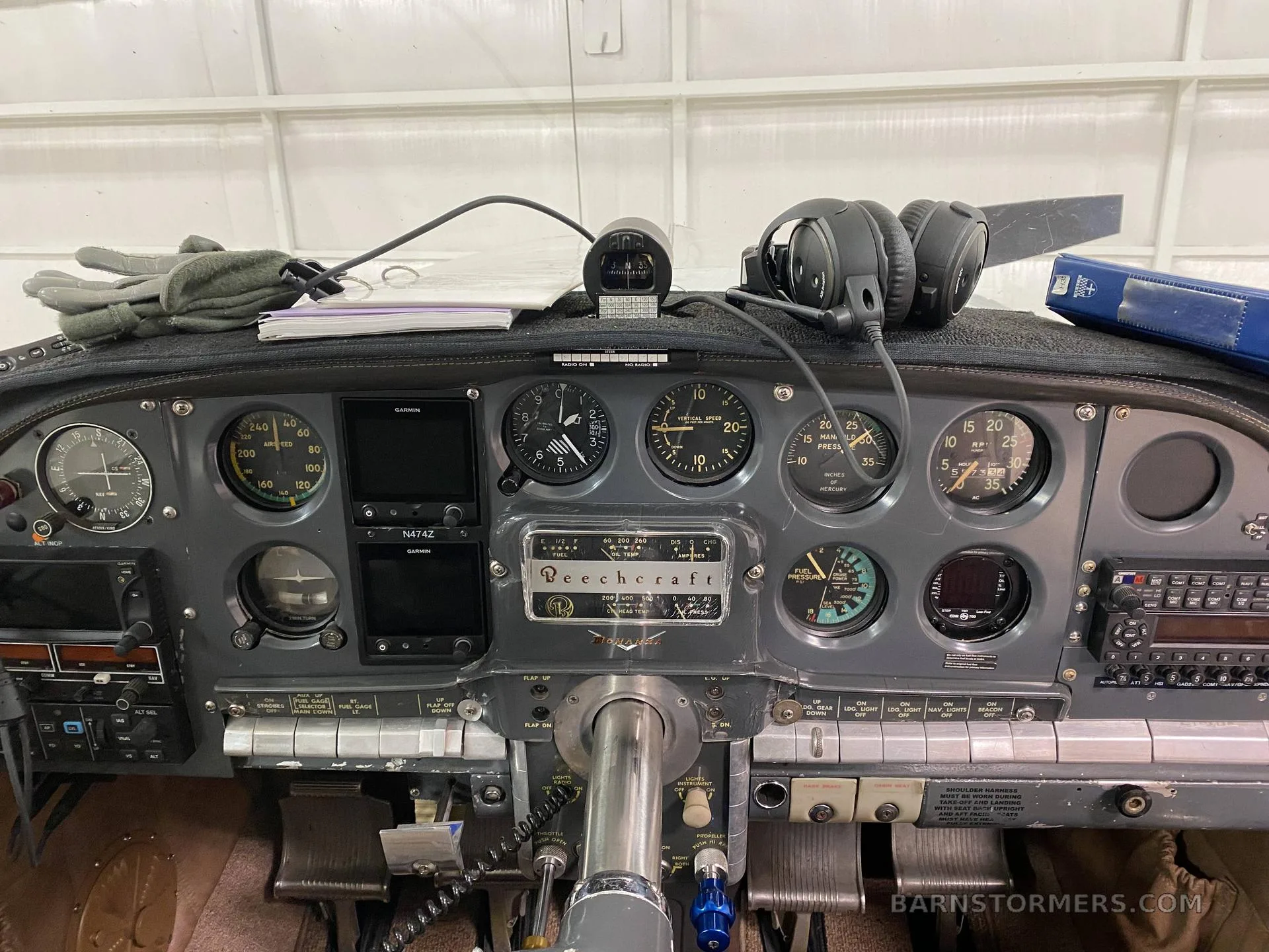 The gray instrument panel of a Beechcraft aircraft, featuring analog gauges and two Garmin displays, is shown with headphones resting on top.