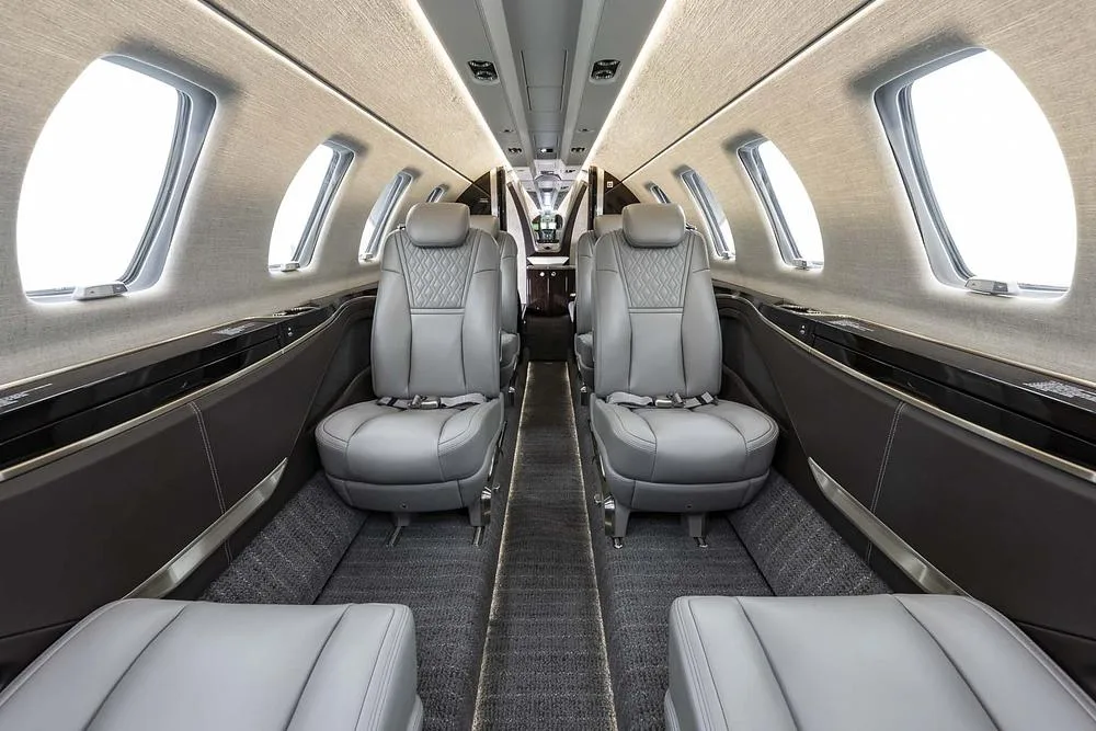 A view of the aircraft's interior cabin featuring grey leather seats and large windows.