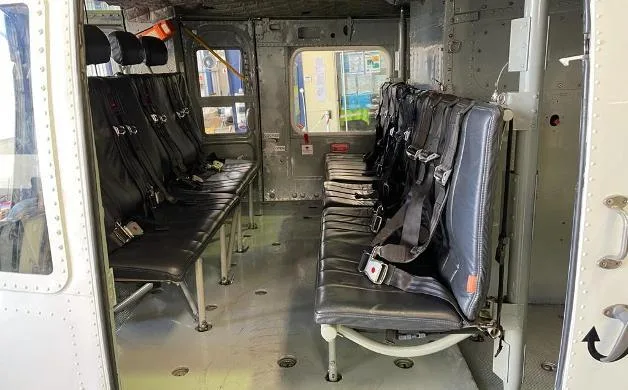 The interior cabin of a helicopter featuring two rows of black bench seats with seatbelts.