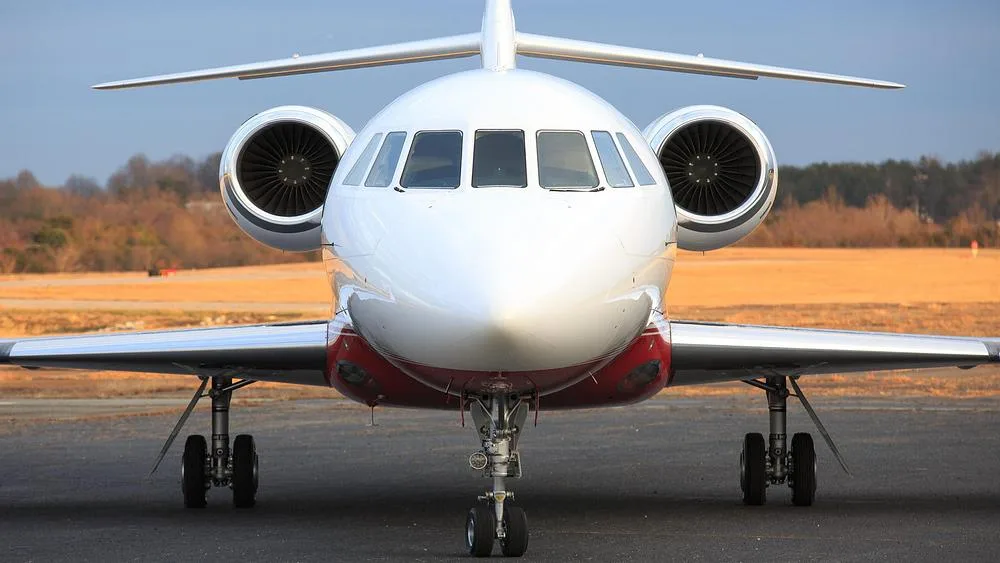 A head-on view of a white and red Dassault Falcon 900 private jet on an airport tarmac.