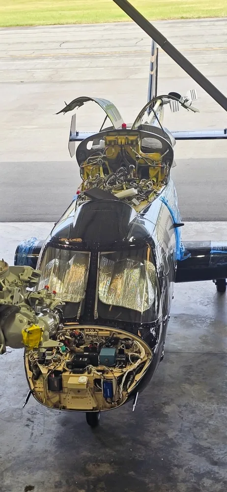 Front view of a black Bell 430 helicopter with maintenance panels open, revealing internal components.