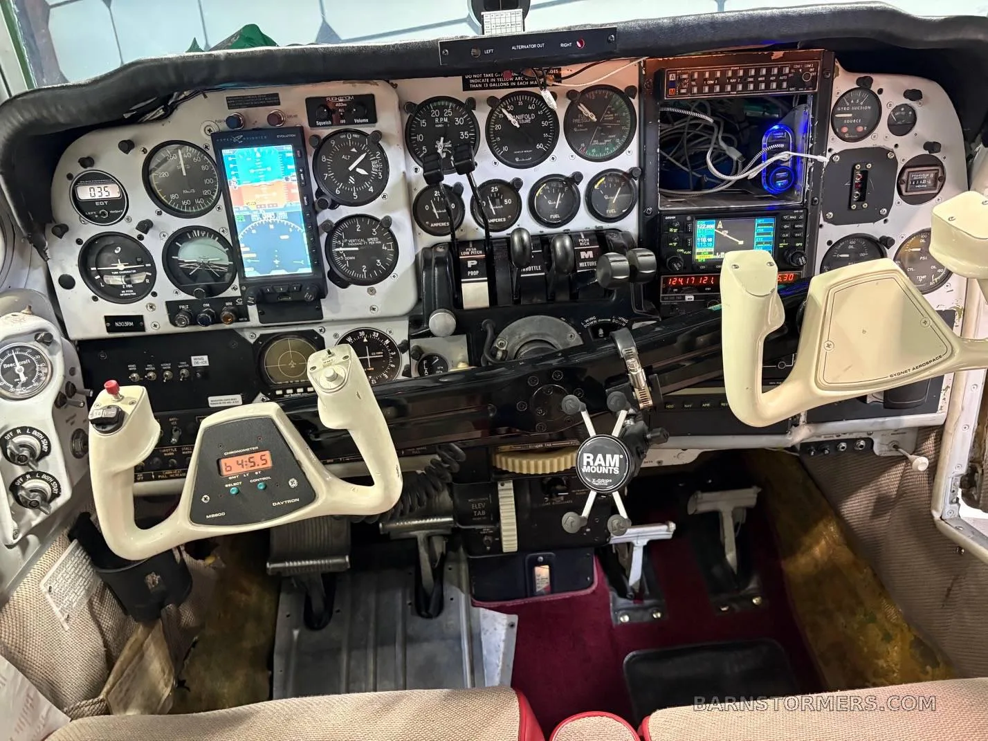 The cockpit of a small aircraft, showing the instrument panel with various gauges, screens, and control yokes.
