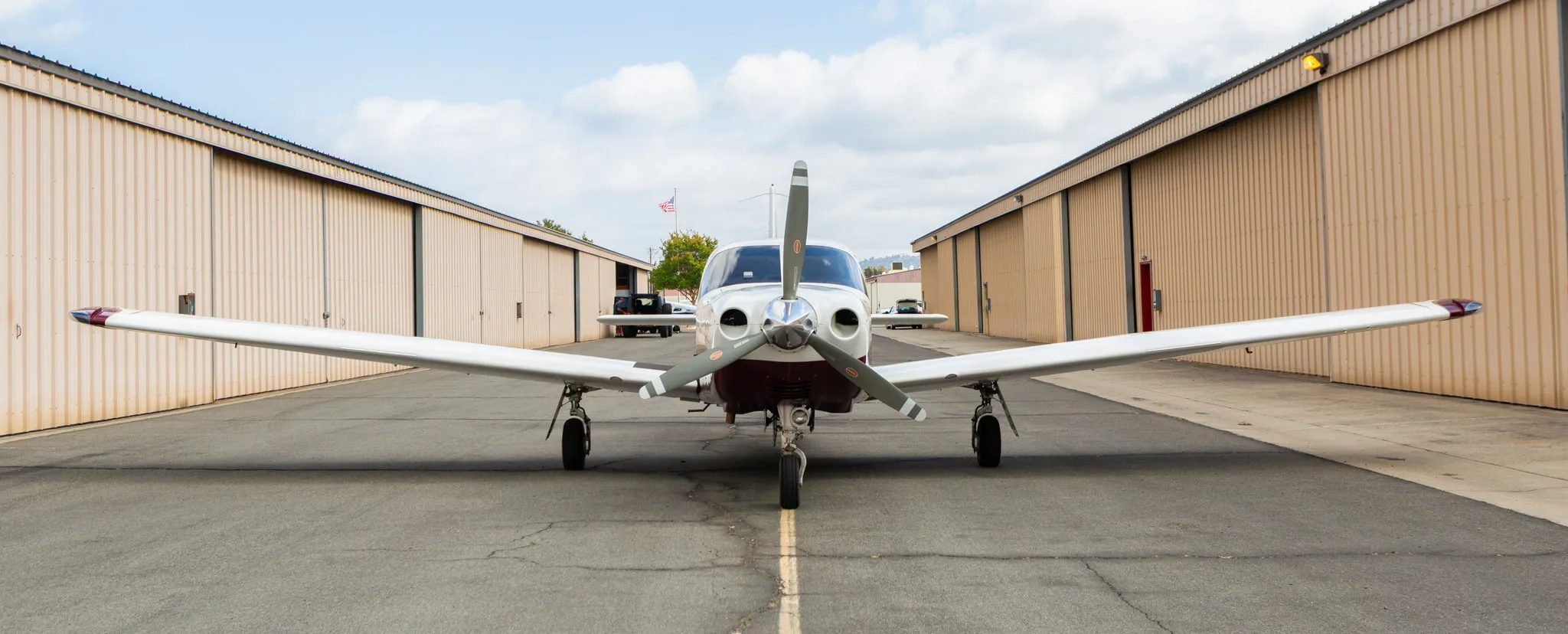 Frontal view of a white and maroon Piper Saratoga II TC aircraft, registration N691MA, parked on an asphalt ramp between hangars.