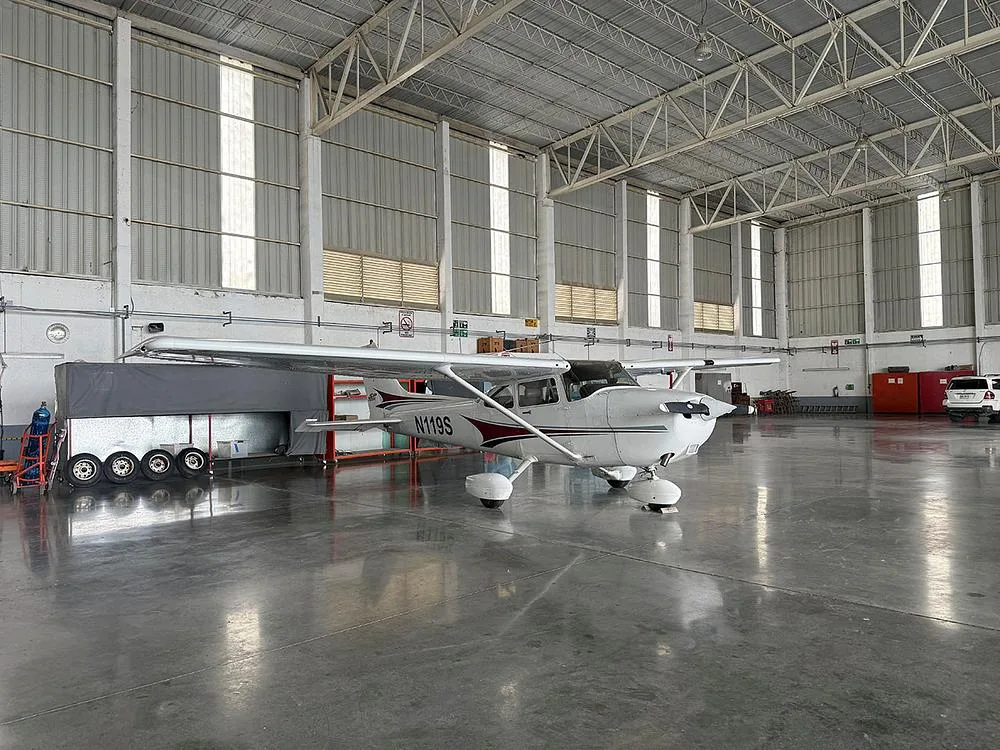 A white Cessna N119S with maroon accents is parked in a hangar, viewed from the front-right.