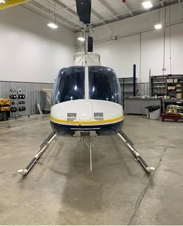 Front view of the white and blue helicopter N94PD with yellow stripes, parked in a hangar.