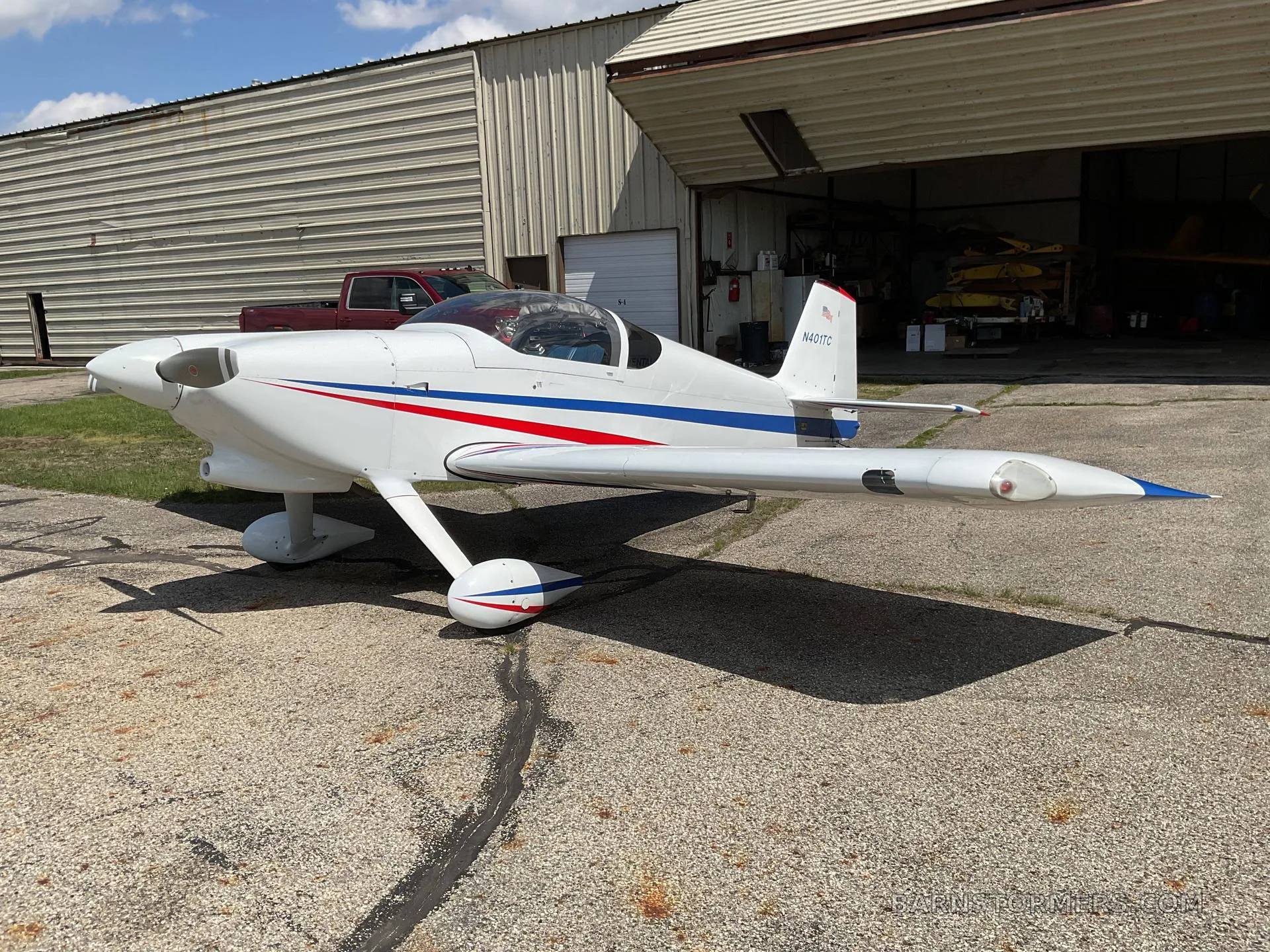 A white single-engine aircraft with a blue stripe (N401TC), parked on an asphalt tarmac in front of an open hangar.