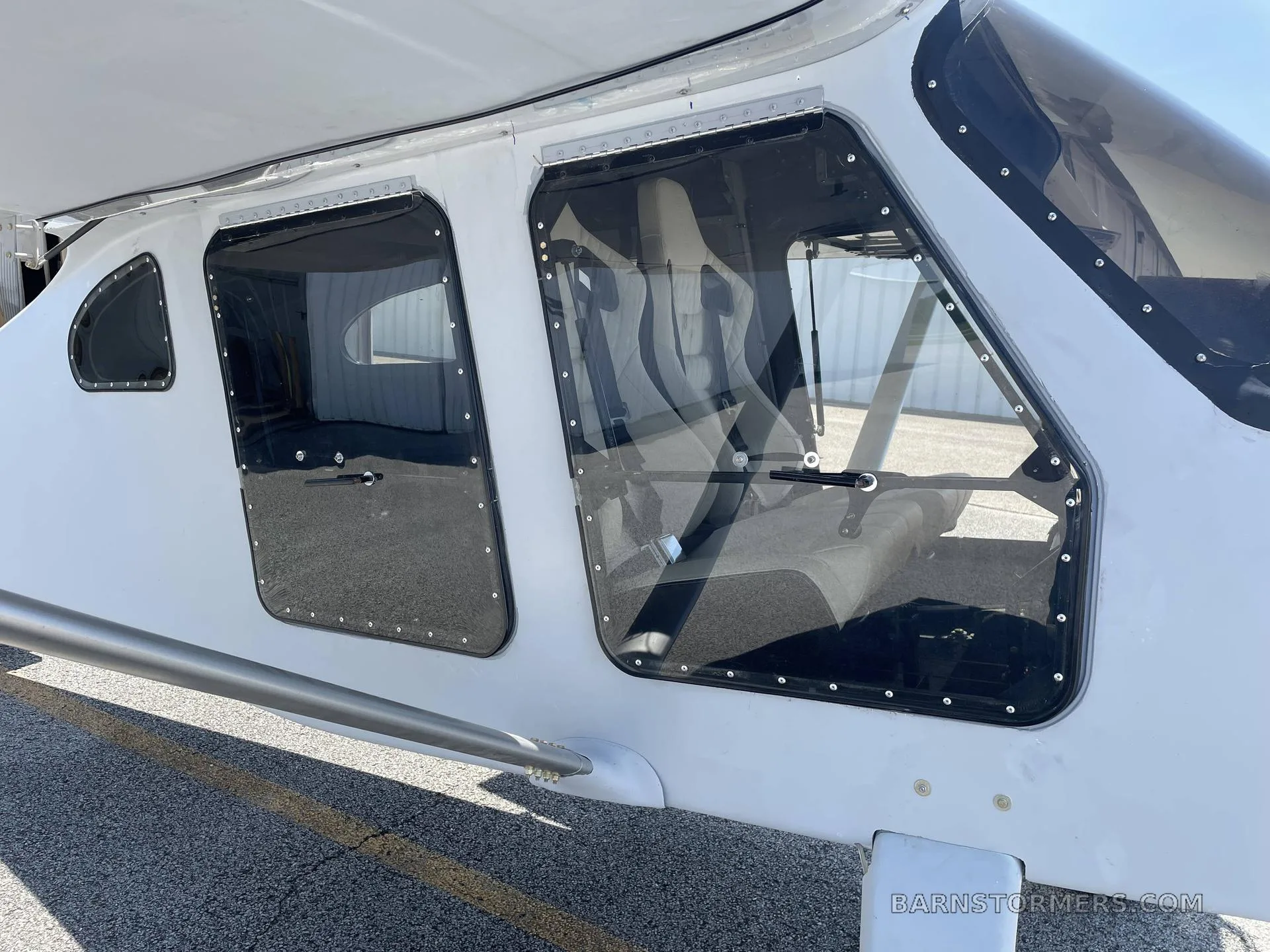 A close-up view of the white aircraft's fuselage shows two large windows and a wing strut.