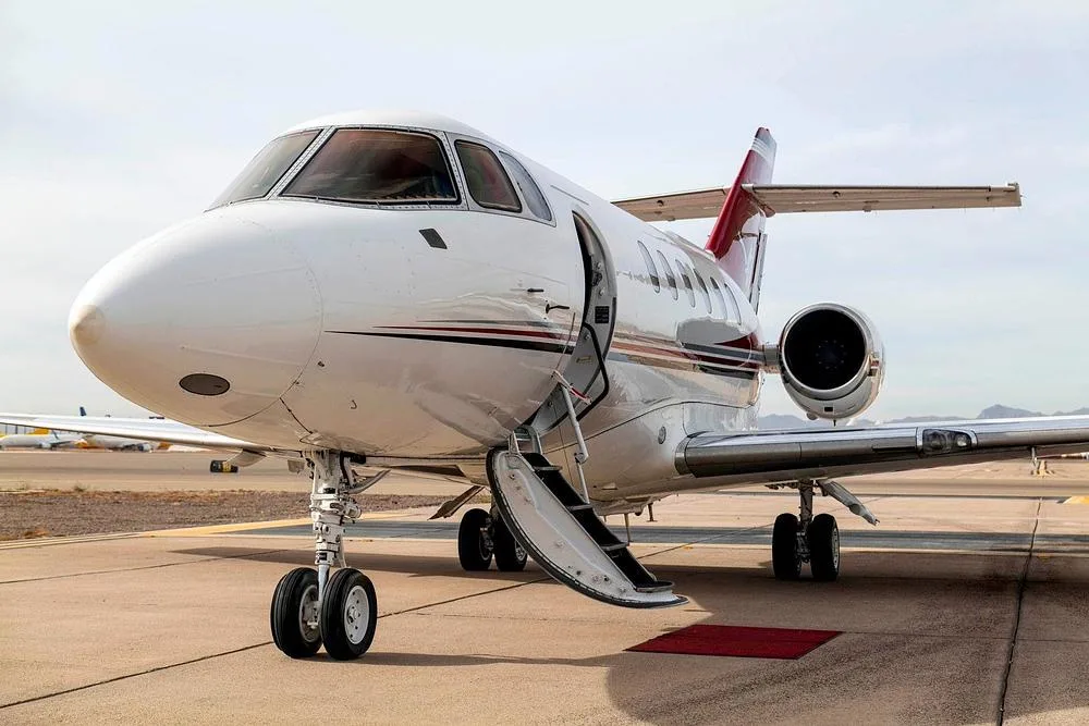 A close-up front view of a white business jet with red and black stripes, showing the open passenger door and stairs.