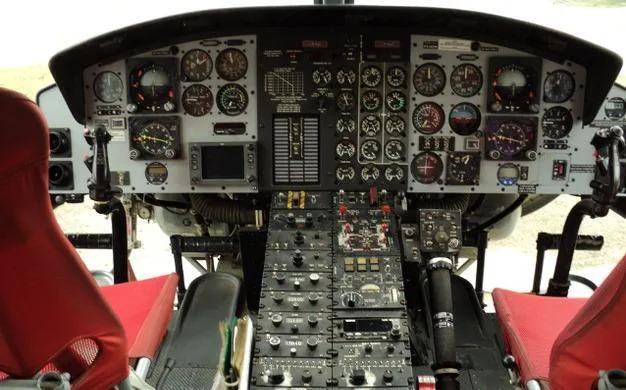 A detailed, head-on view of a helicopter's complex instrument panel and central control console with many gauges and switches.