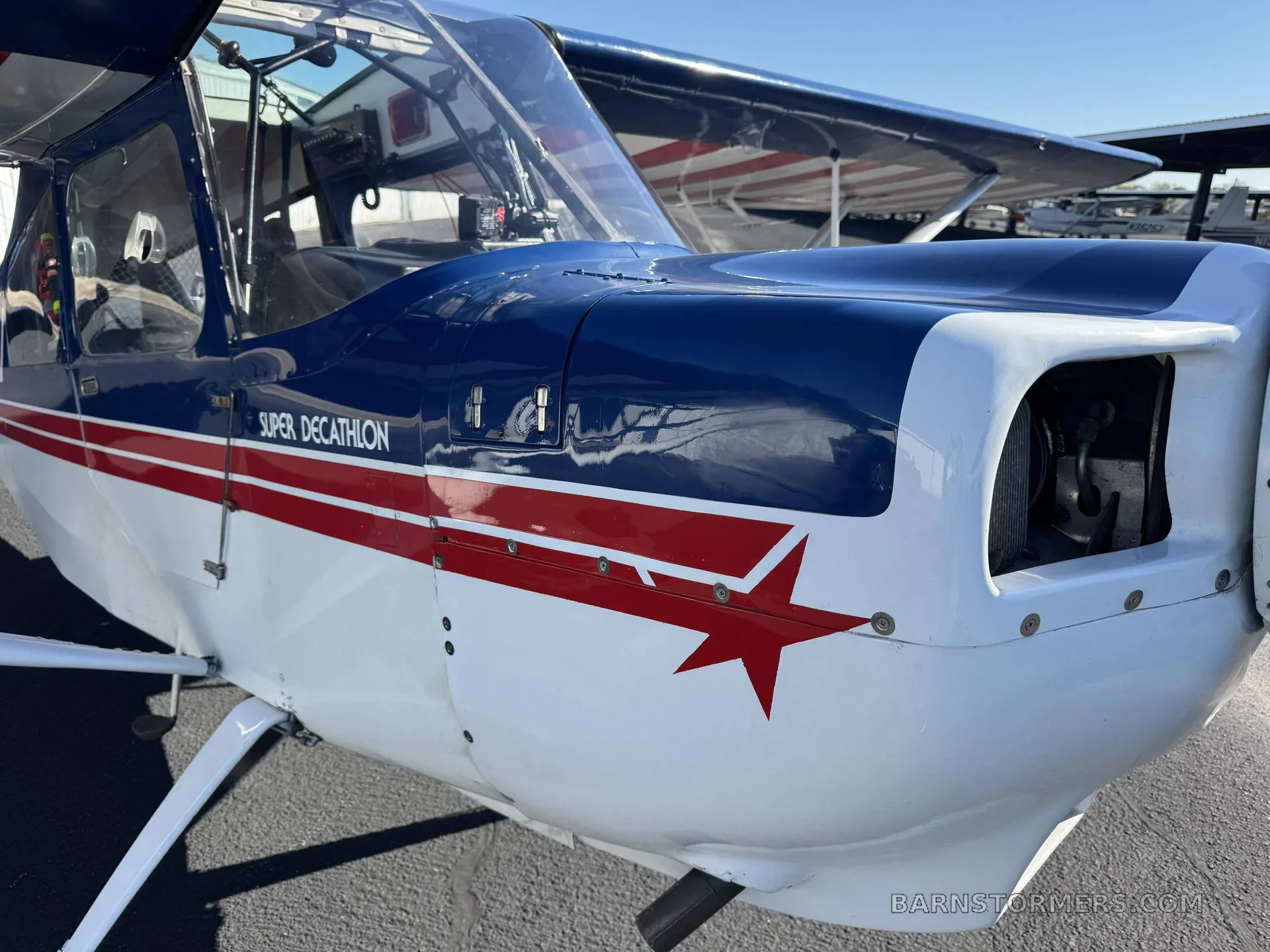 A close-up view of the nose of a blue and white Super Decathlon aircraft with a red stripe and star.