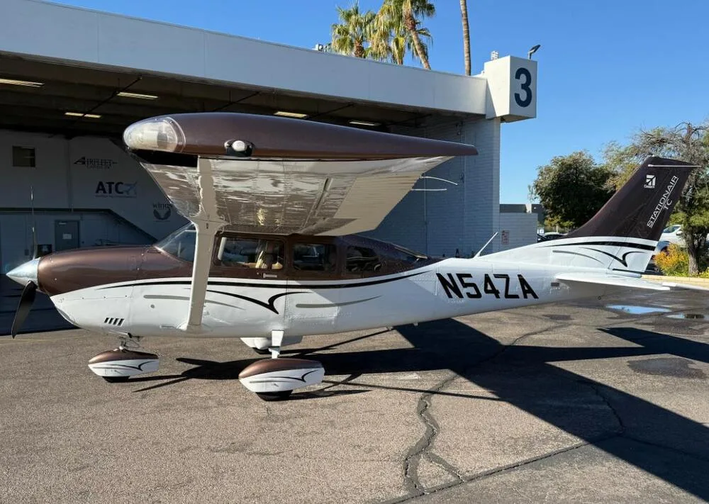 A brown and white Cessna 206 Stationair aircraft (N54ZA) parked on a tarmac next to a hangar.