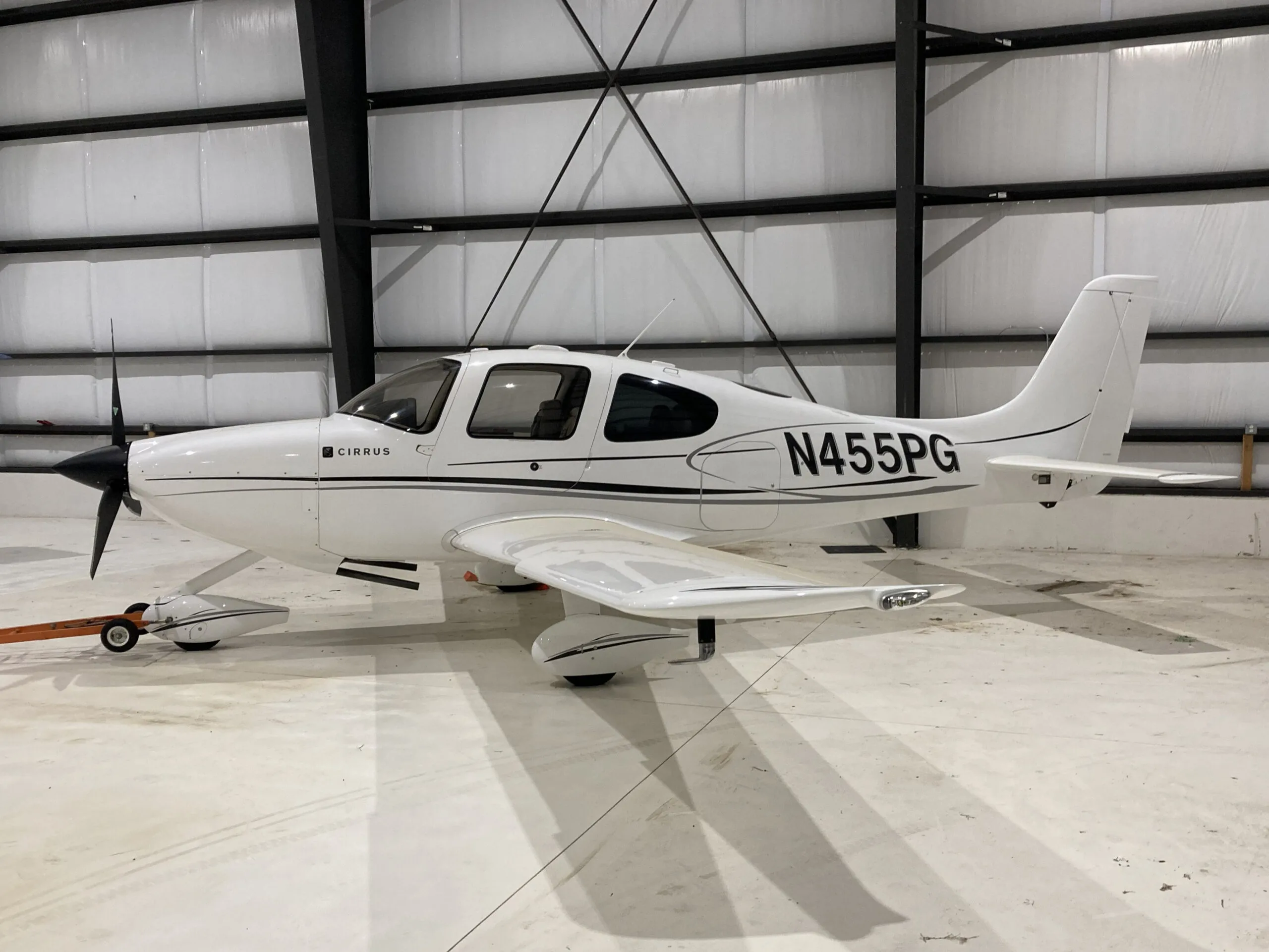 A white Cirrus SR22 aircraft with black and grey stripes, registration N455PG, parked in a hangar.