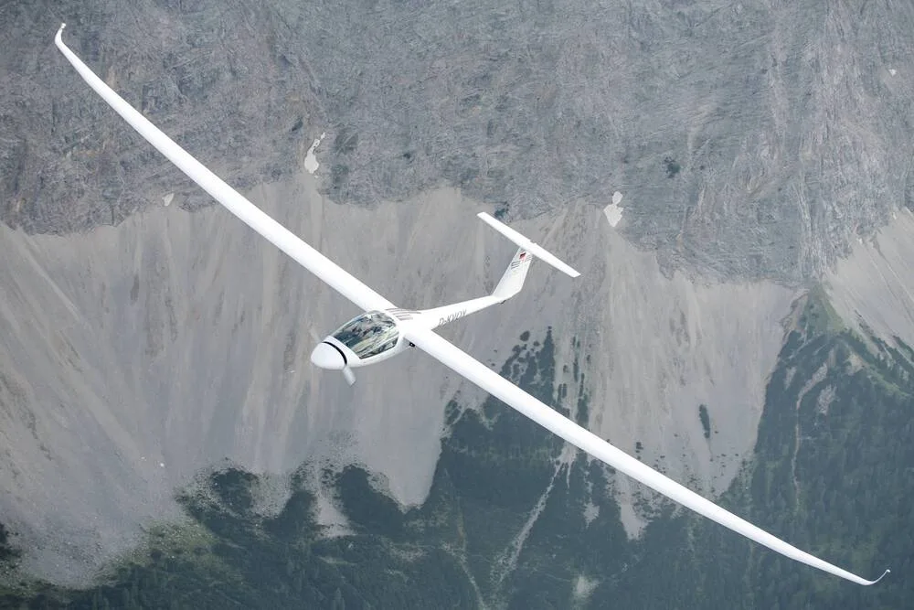 A white Stemme S12 motorglider with registration D-KWW in flight over a rocky mountain range.