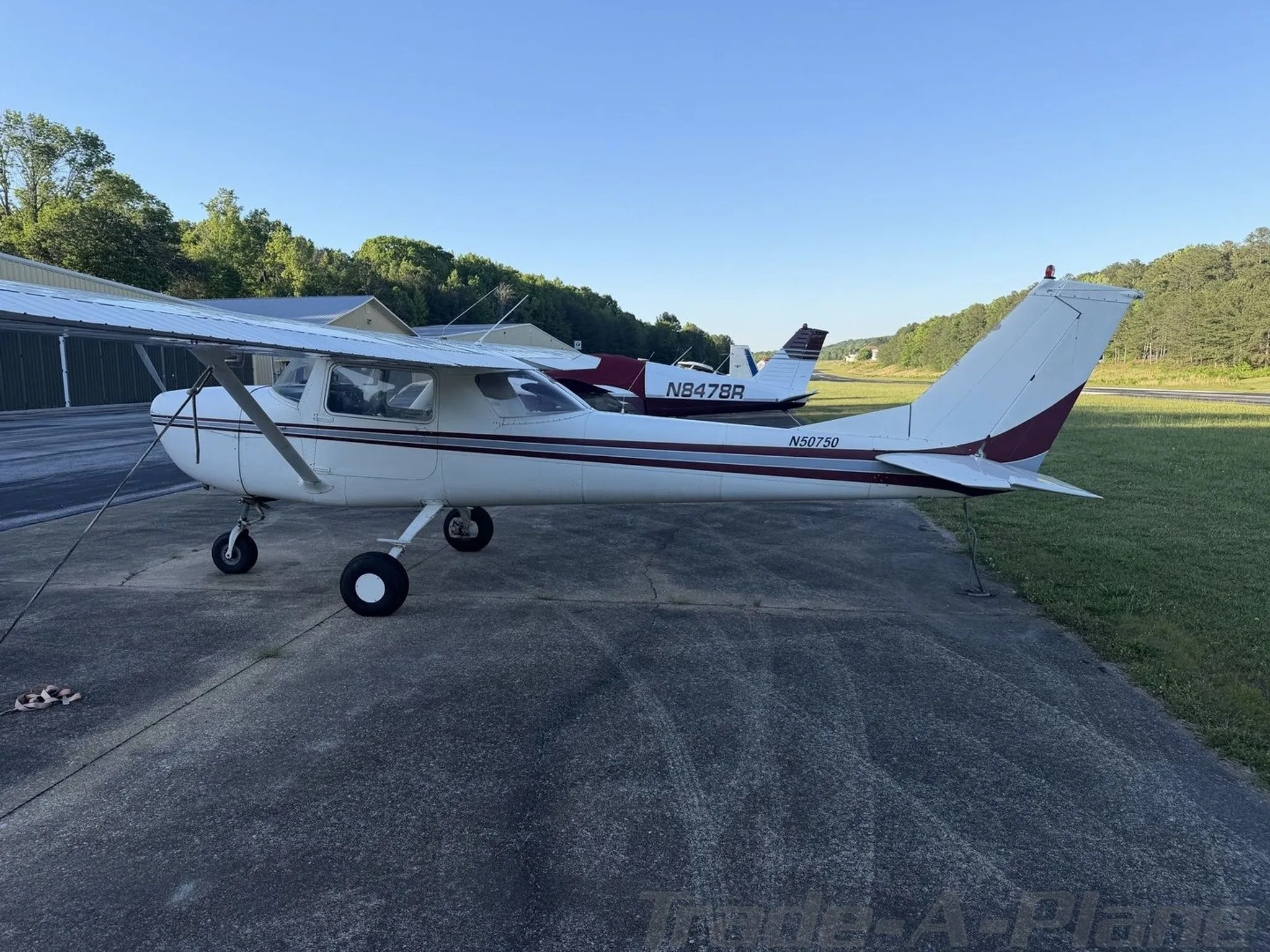 Side view of a white Cessna 172 with maroon stripes (N50750) parked on a tarmac next to another aircraft.