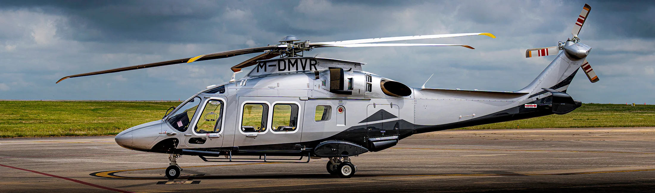 The M-DMVR helicopter is parked on the tarmac with a cloudy sky in the background.