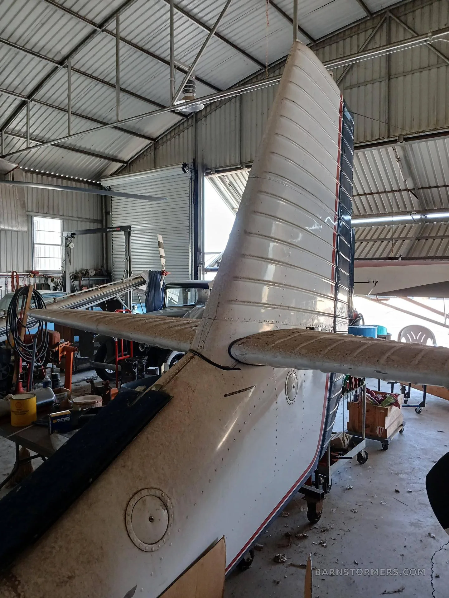 Rear view of the tail and horizontal stabilizer of a white, red, and blue amphibious aircraft inside a hangar.
