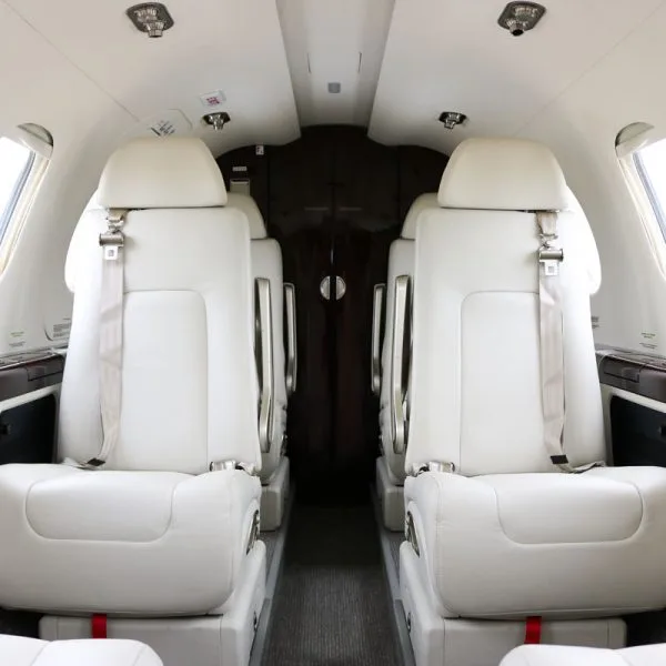 The interior cabin of a private jet with four white leather seats facing each other.