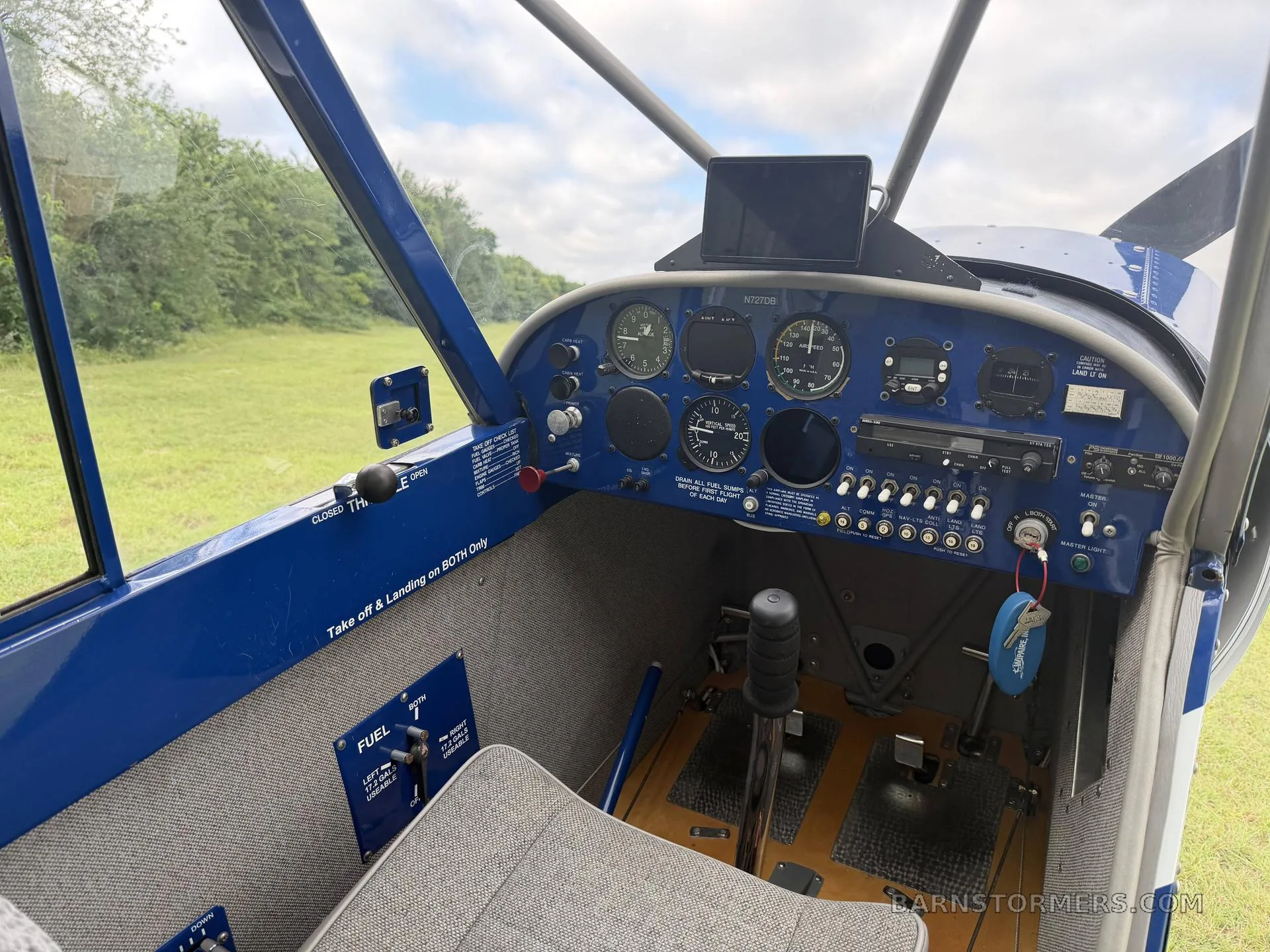 The blue instrument panel and controls of a small aircraft cockpit, with a view of a grassy field outside.