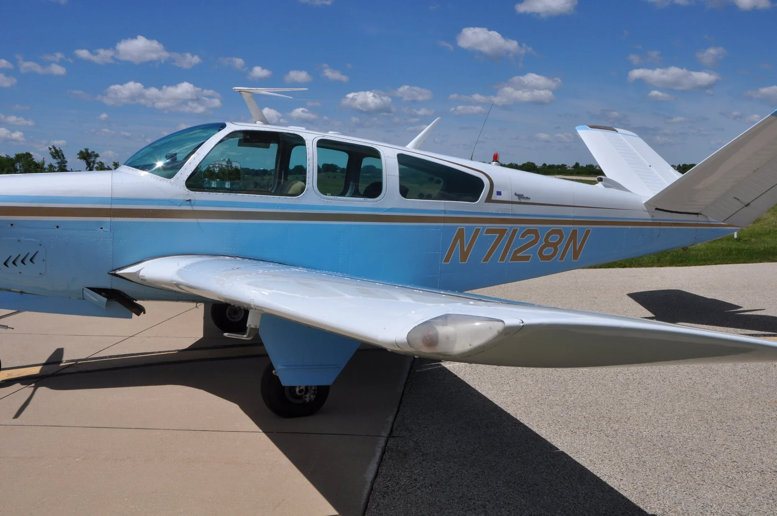 A close-up of the fuselage and wing of a light blue and white single-engine aircraft, showing the registration N7128N.