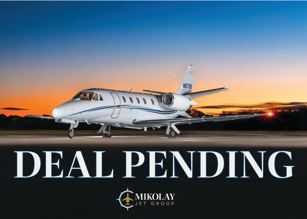 A white Cessna Citation private jet with blue stripes is parked on a runway at sunset.