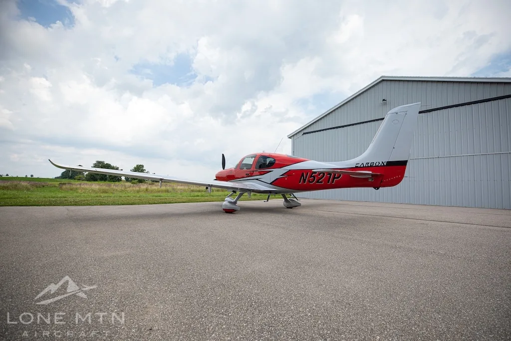 A red and silver Cirrus SR22 aircraft, N521P, seen from the rear-right, parked on an asphalt ramp.