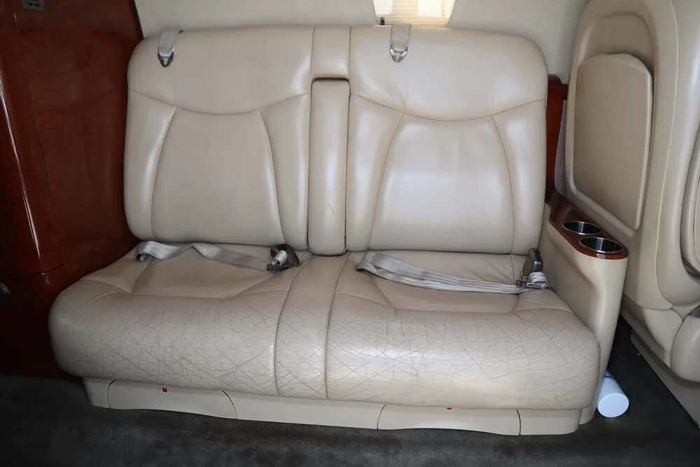 A close-up view of a two-person beige leather bench seat in the aircraft cabin, showing some wear.
