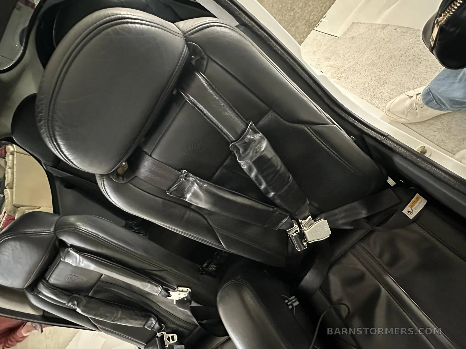 Close-up view of black leather aircraft seats with seatbelts, showing the cabin interior.