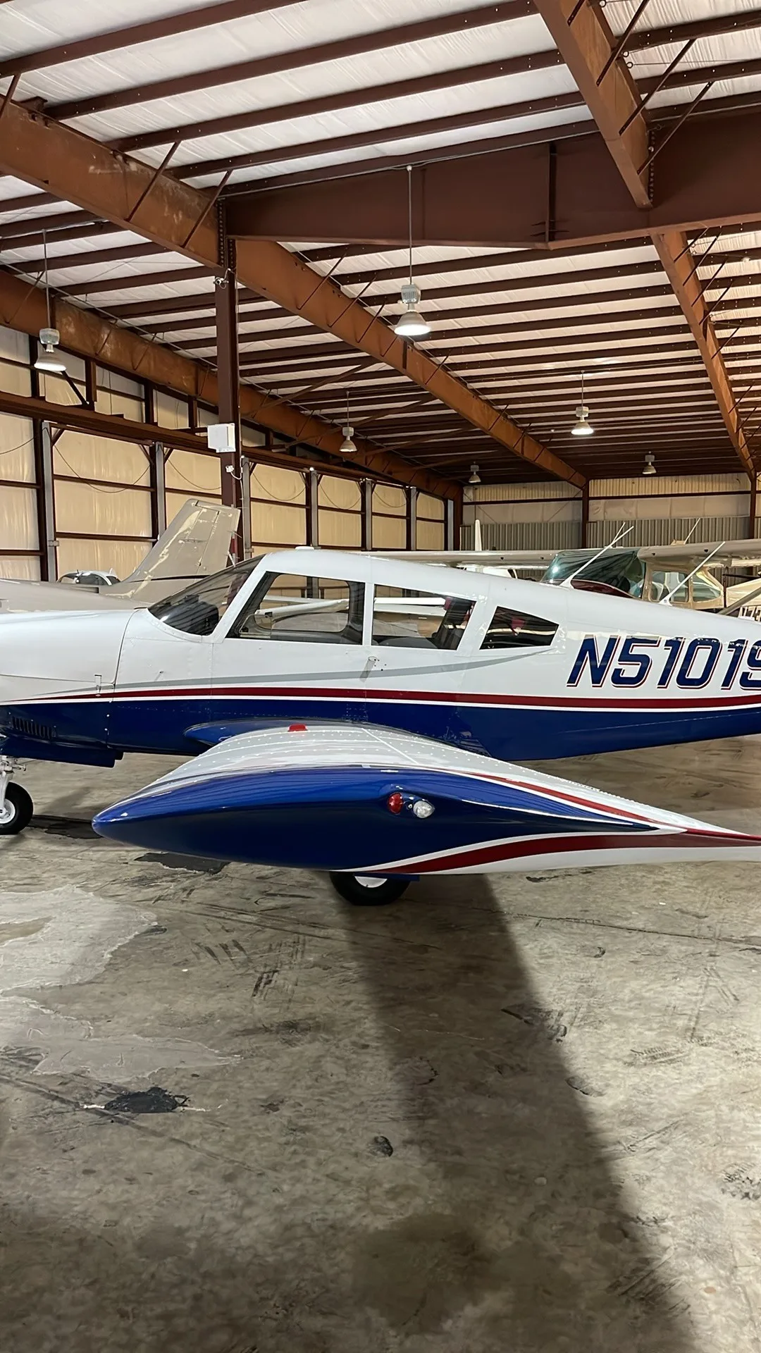 A side view of the white and blue Piper PA-28-180 Cherokee Challenger (N5101S) parked inside a hangar.