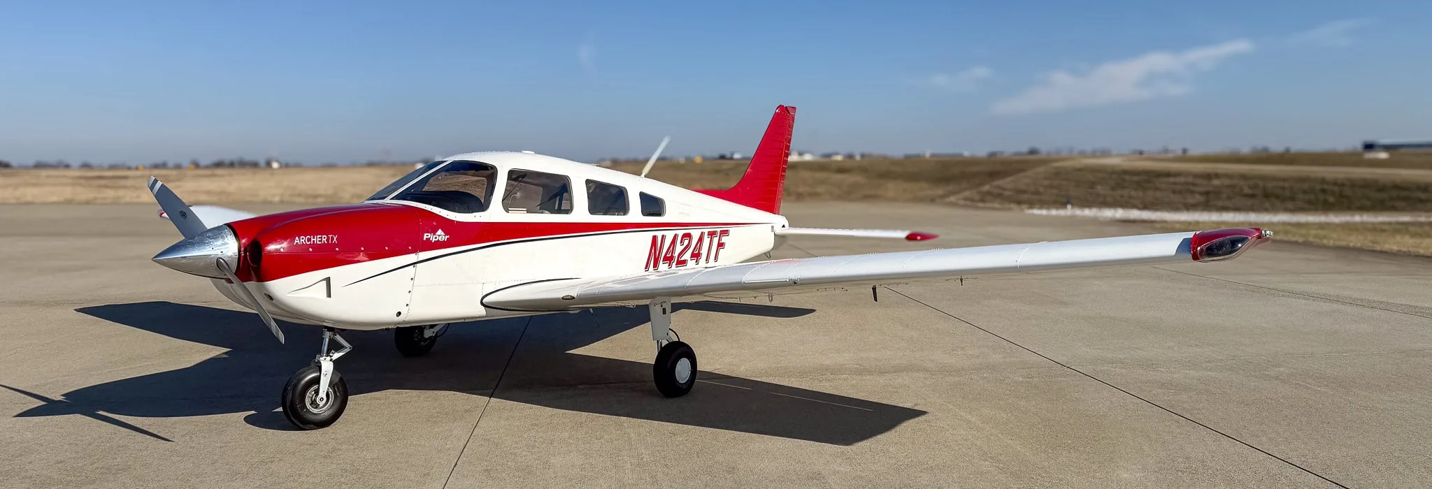 A white Piper Archer TX with red accents and tail number N424TF parked on an airfield.