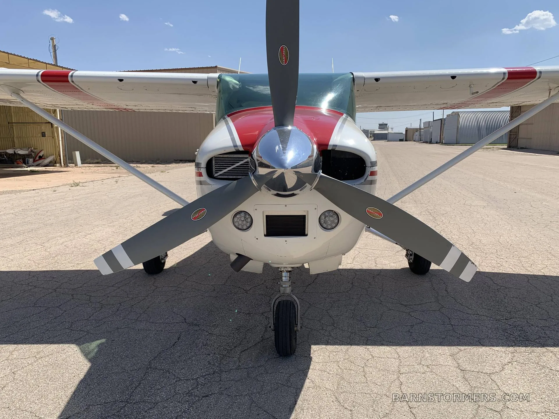 Front view of a white and red single-engine propeller aircraft with a chrome spinner, parked on an asphalt ramp.