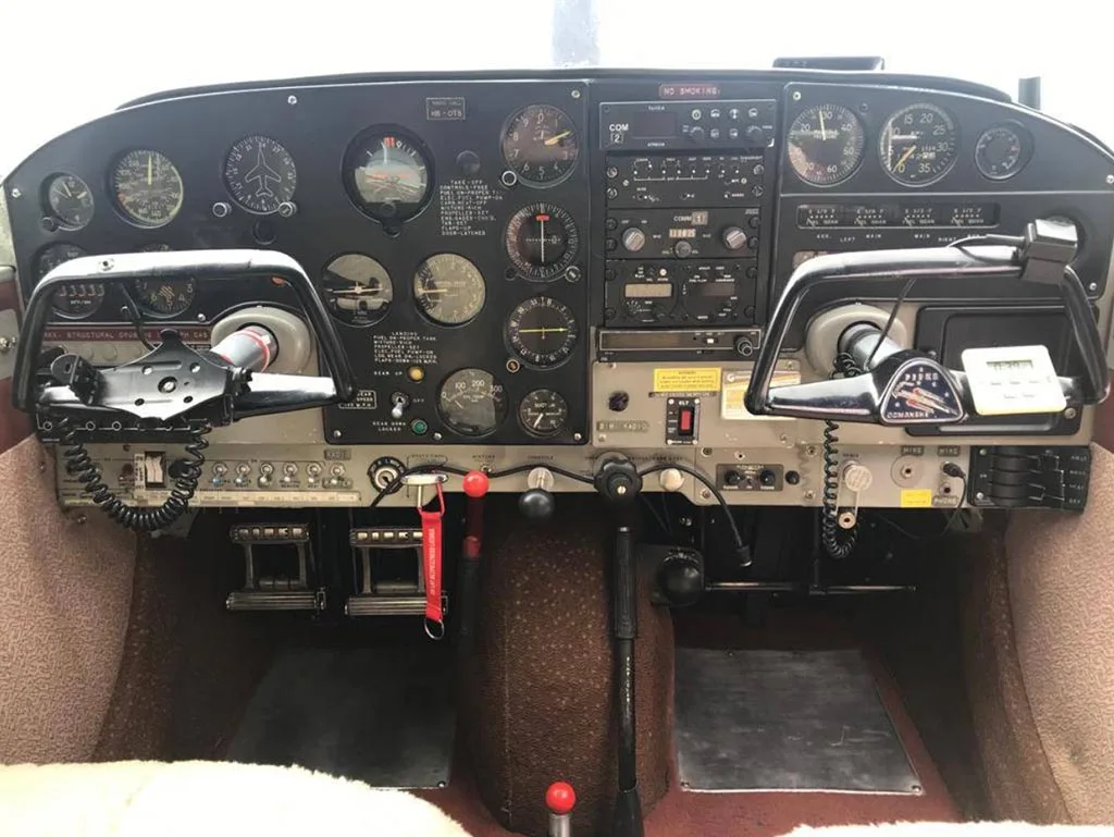 The cockpit of a small aircraft, featuring a black instrument panel with various gauges and two control yokes.