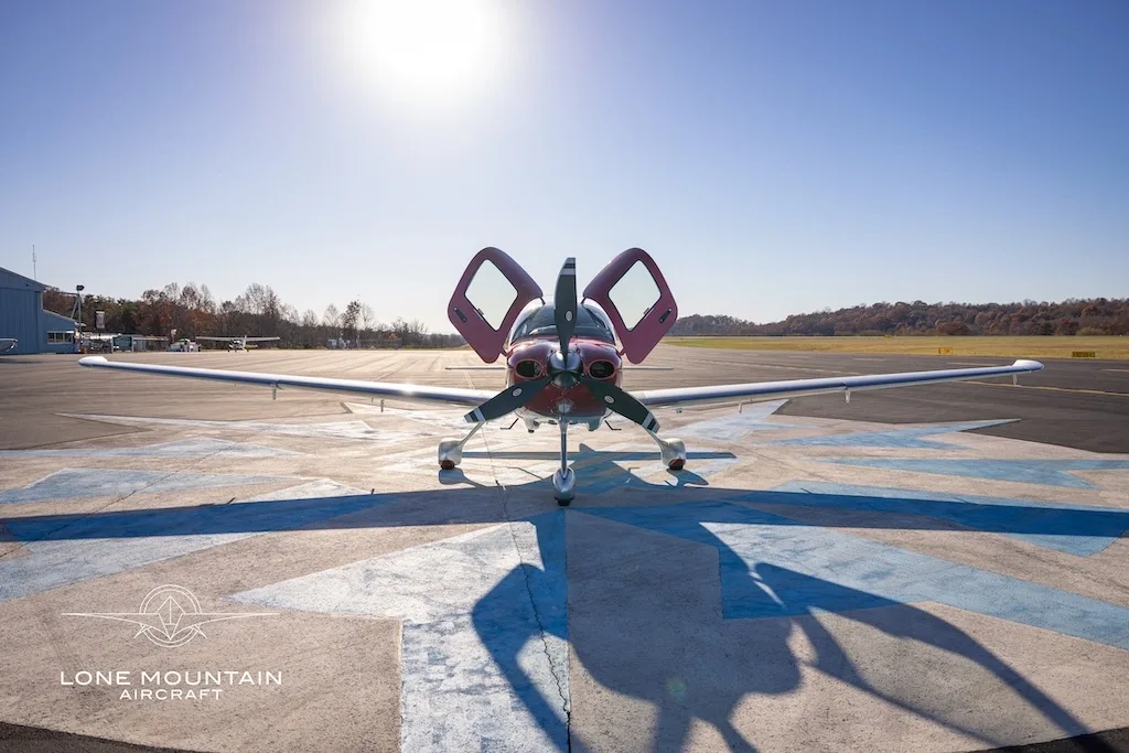 A front view of a red and white Cirrus SR22 aircraft with registration N5785C parked on an airfield with its doors open.