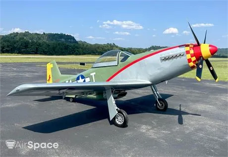 A P-51 Mustang-style warbird with olive green, silver, and red paint, and a checkered nose, sits on an airfield tarmac.