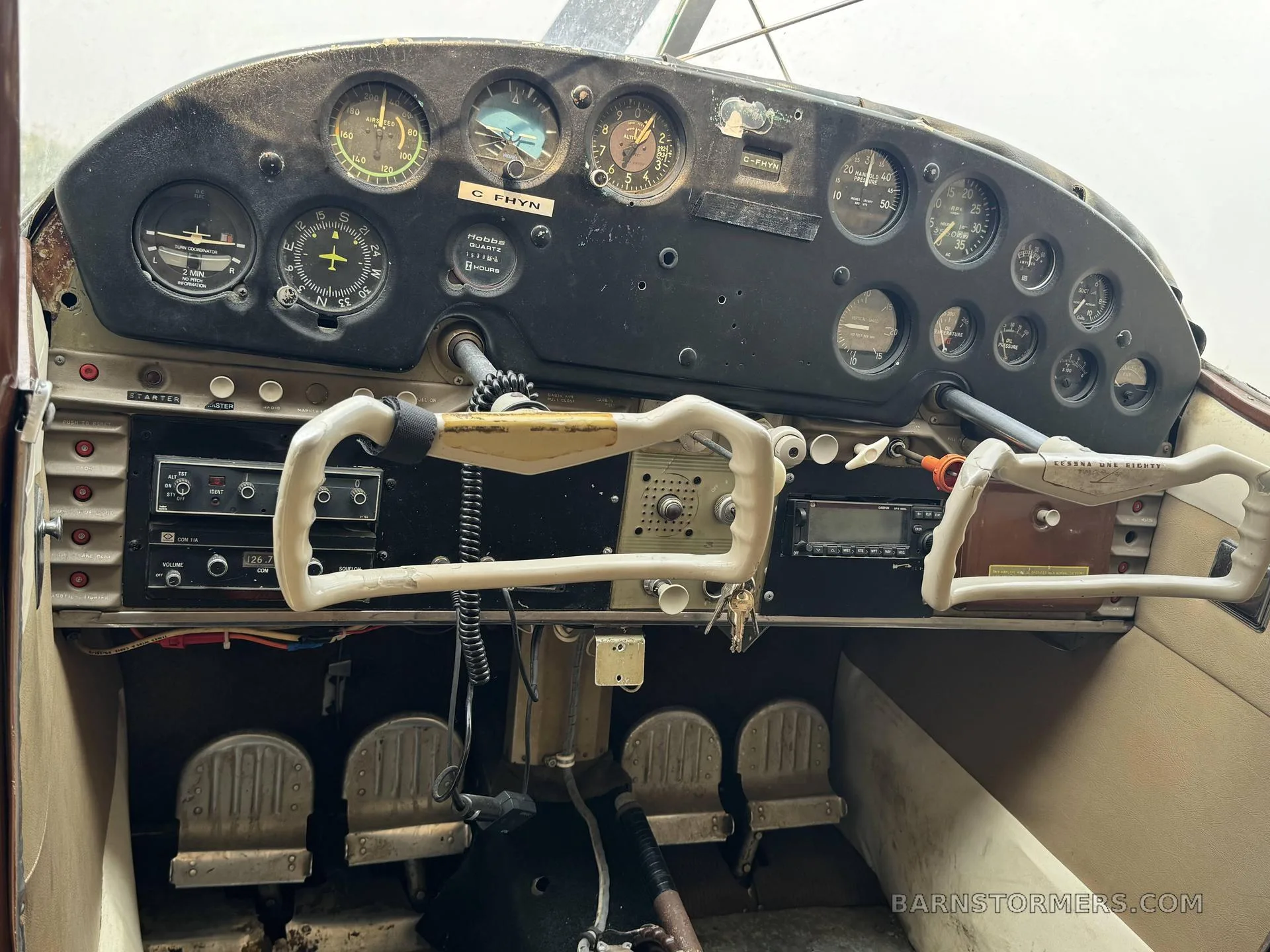 A close-up view of the worn instrument panel and controls of a Cessna 180 cockpit.