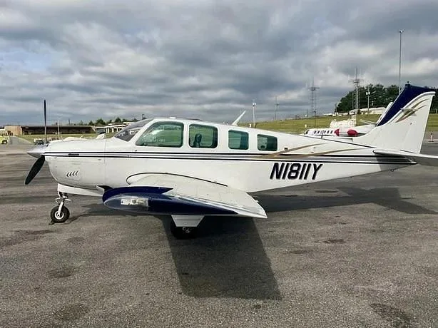 A white single-engine aircraft with dark blue and gold accents, registration N1811Y, parked on an asphalt ramp under a cloudy sky.