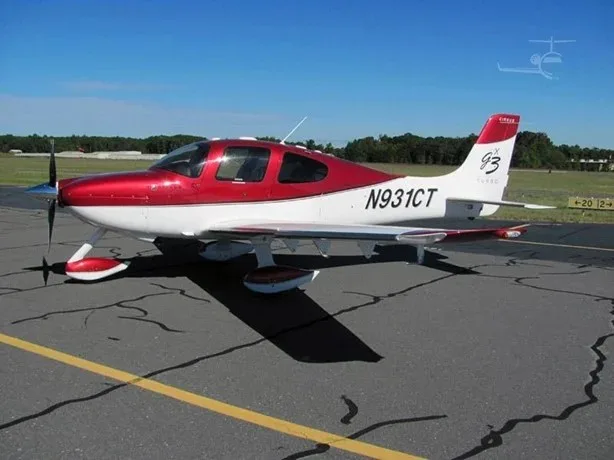A side view of a red and white Cirrus SR22T aircraft, N931CT, parked on an airfield under a clear sky.