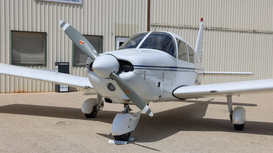 Front-side view of the white Piper Cherokee 180 (N9560J) showing the propeller and cockpit.