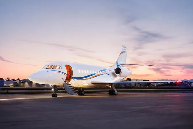 A white business jet with blue and orange stripes is parked on an tarmac with its door open at sunset.
