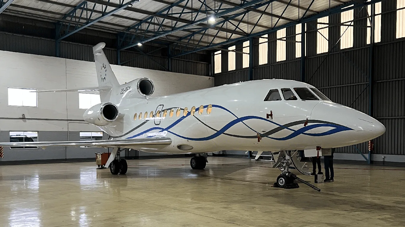 A white Dassault Falcon 900EX business jet with blue and grey wavy stripes is parked inside a hangar.