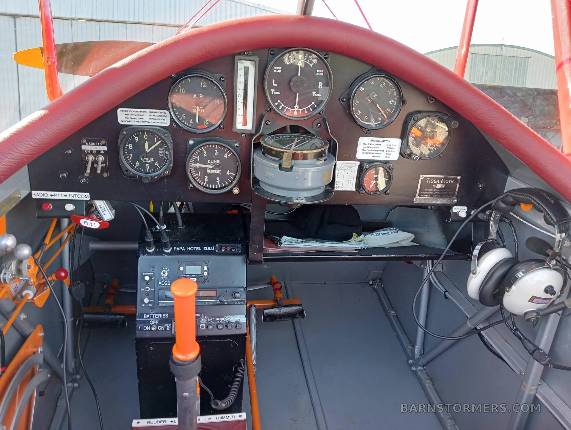 The cockpit of a biplane features a red padded dashboard, various analog gauges, a radio, and a control stick.