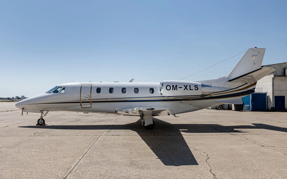 A white Cessna Citation XLS business jet with gold and black stripes is parked on a tarmac under a clear blue sky.