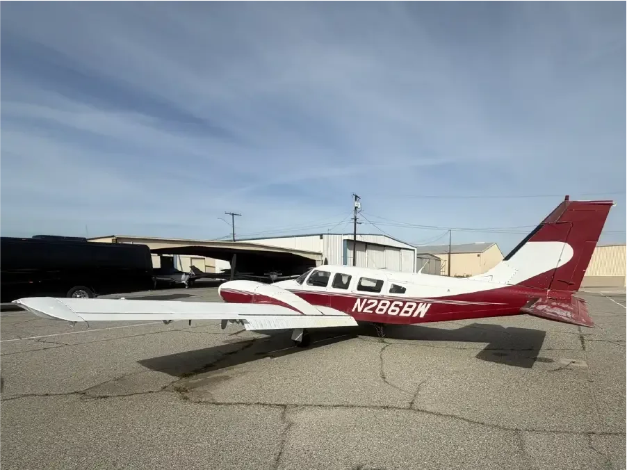 A white and red single-engine propeller aircraft, registration N286BW, parked on an asphalt apron with hangars in the background.