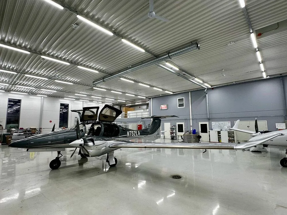 A full side view of a gray and silver Diamond DA62 aircraft with registration N752LA, parked in a hangar with its doors open.