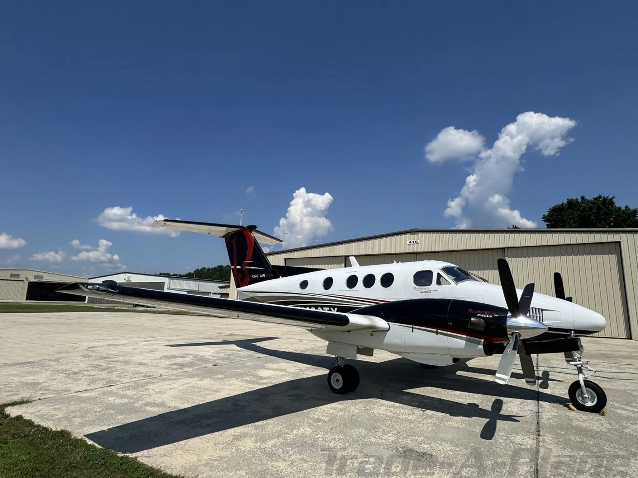 A three-quarter front view of a white and black Beechcraft King Air F90, N490TX, parked on a tarmac with a hangar in the background.