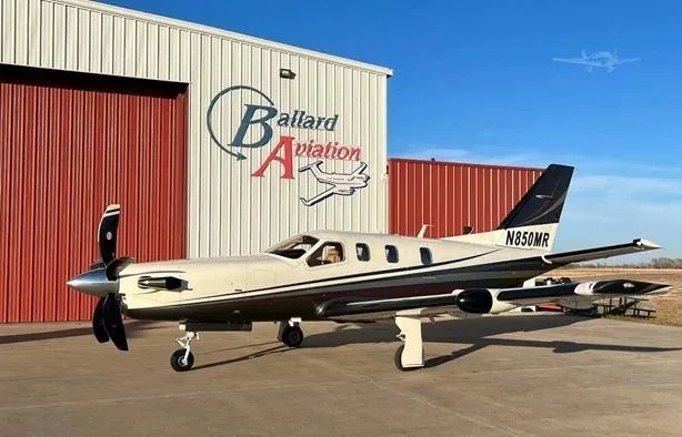 A white and black single-engine turboprop aircraft, N850MR, is parked on an tarmac in front of a hangar.