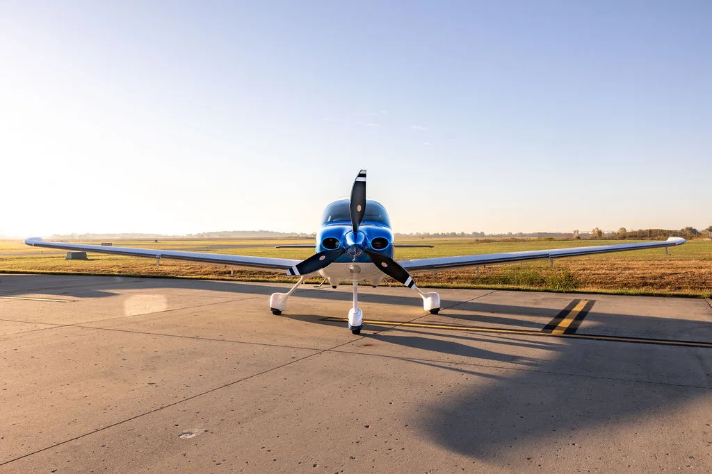 A front view of a blue and white Cirrus SR22 aircraft parked on an airfield.
