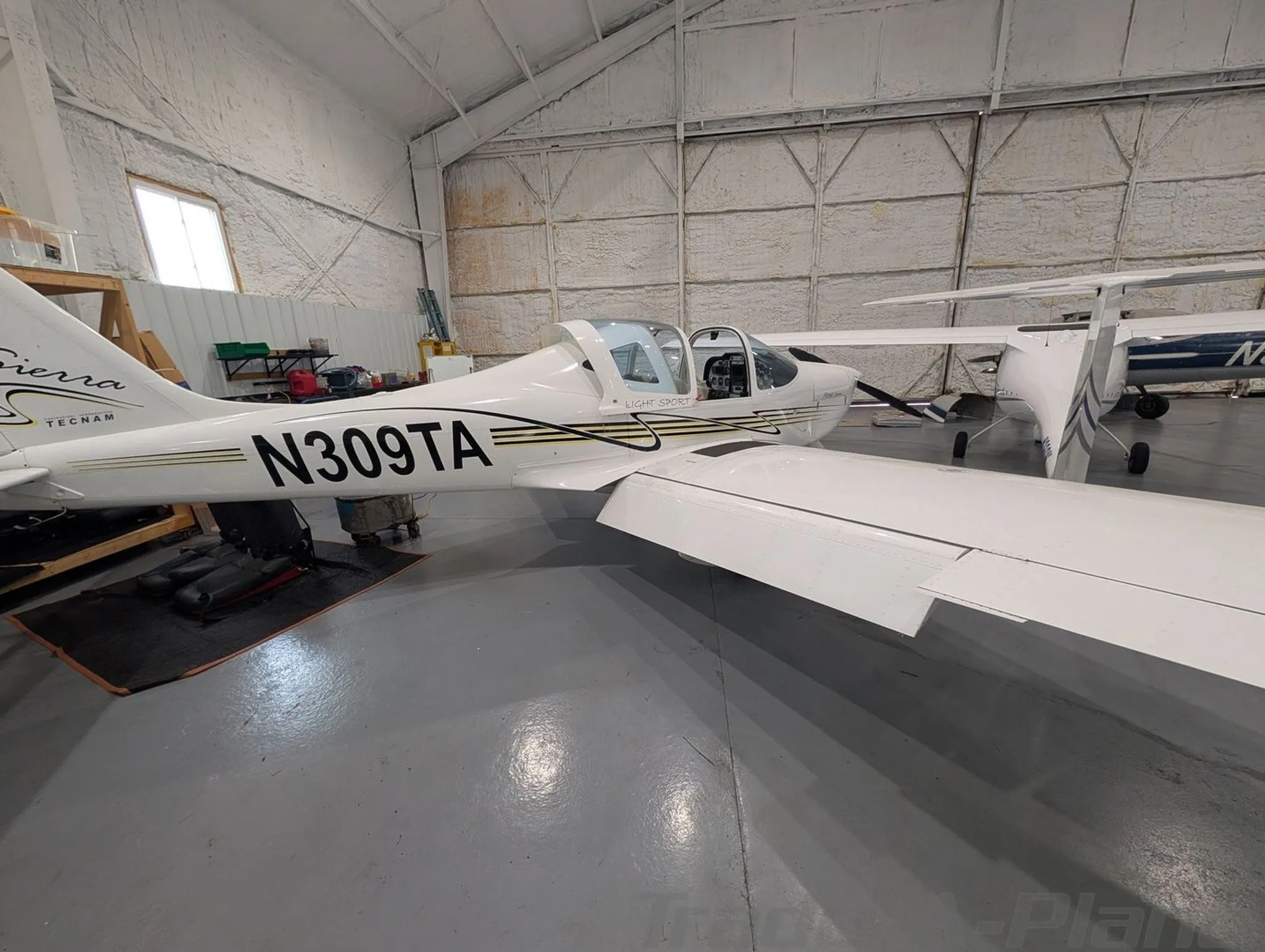 A side view of the white Tecnam P2002 Sierra N309TA, showing its tail and wing in a hangar.