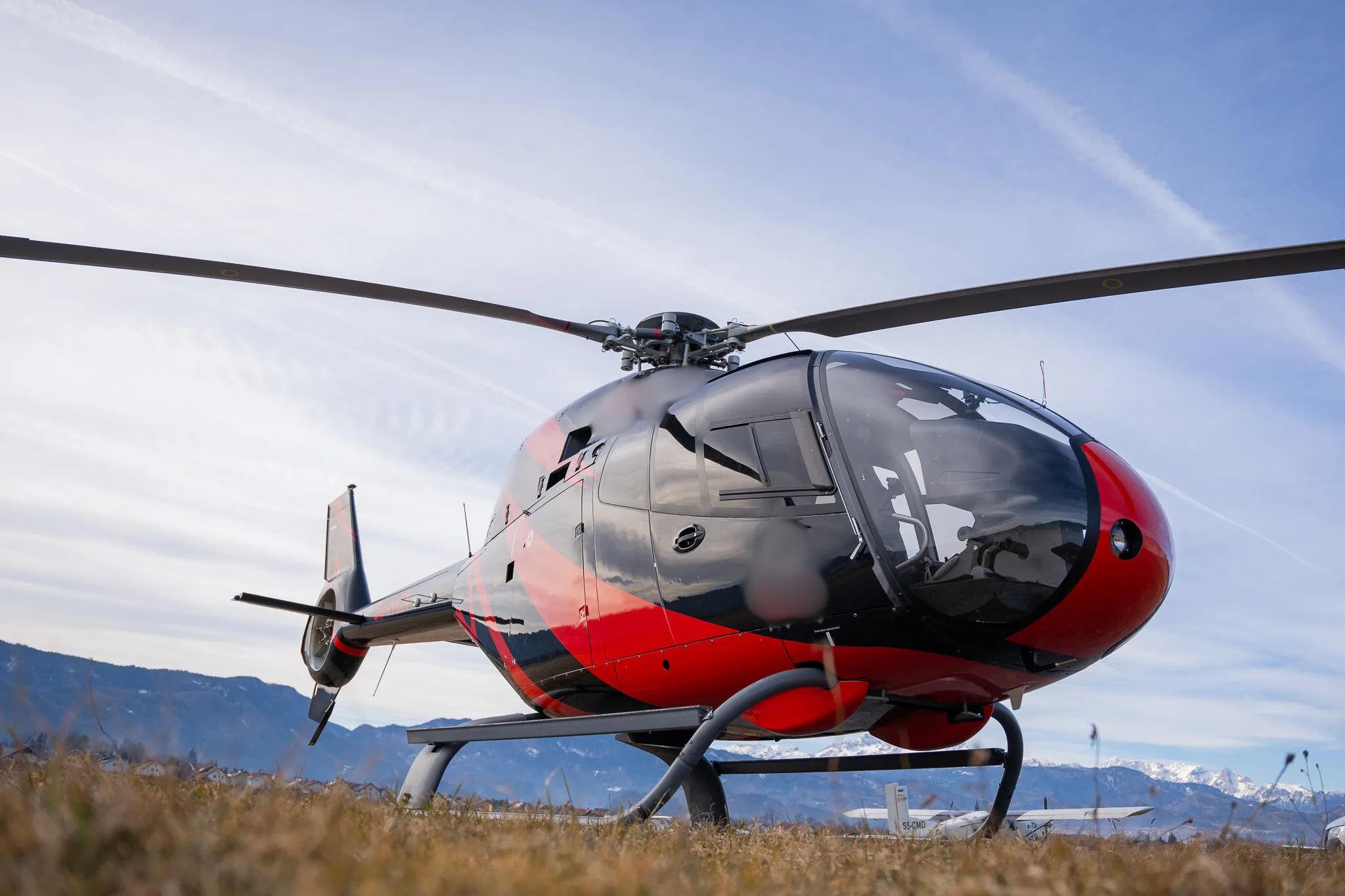 A black and red helicopter sits on the ground with mountains in the background.